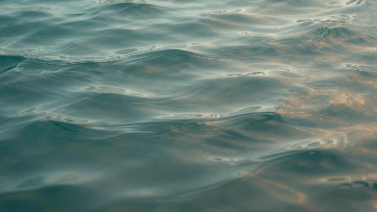 Fotografía abstracta de seda ondulada en tonos verde agua y ámbar, metáfora del drenaje linfático sin diagramas ni dispositivos.